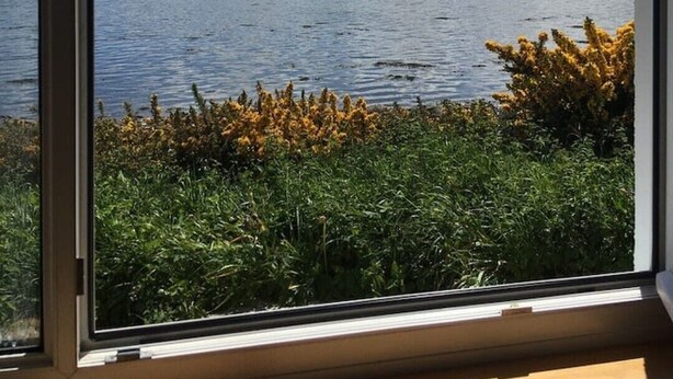 Una ventana con vista a un lago y colinas distantes.