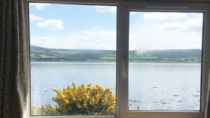 Una habitación con un amplio ventanal con vistas a un lago y colinas.