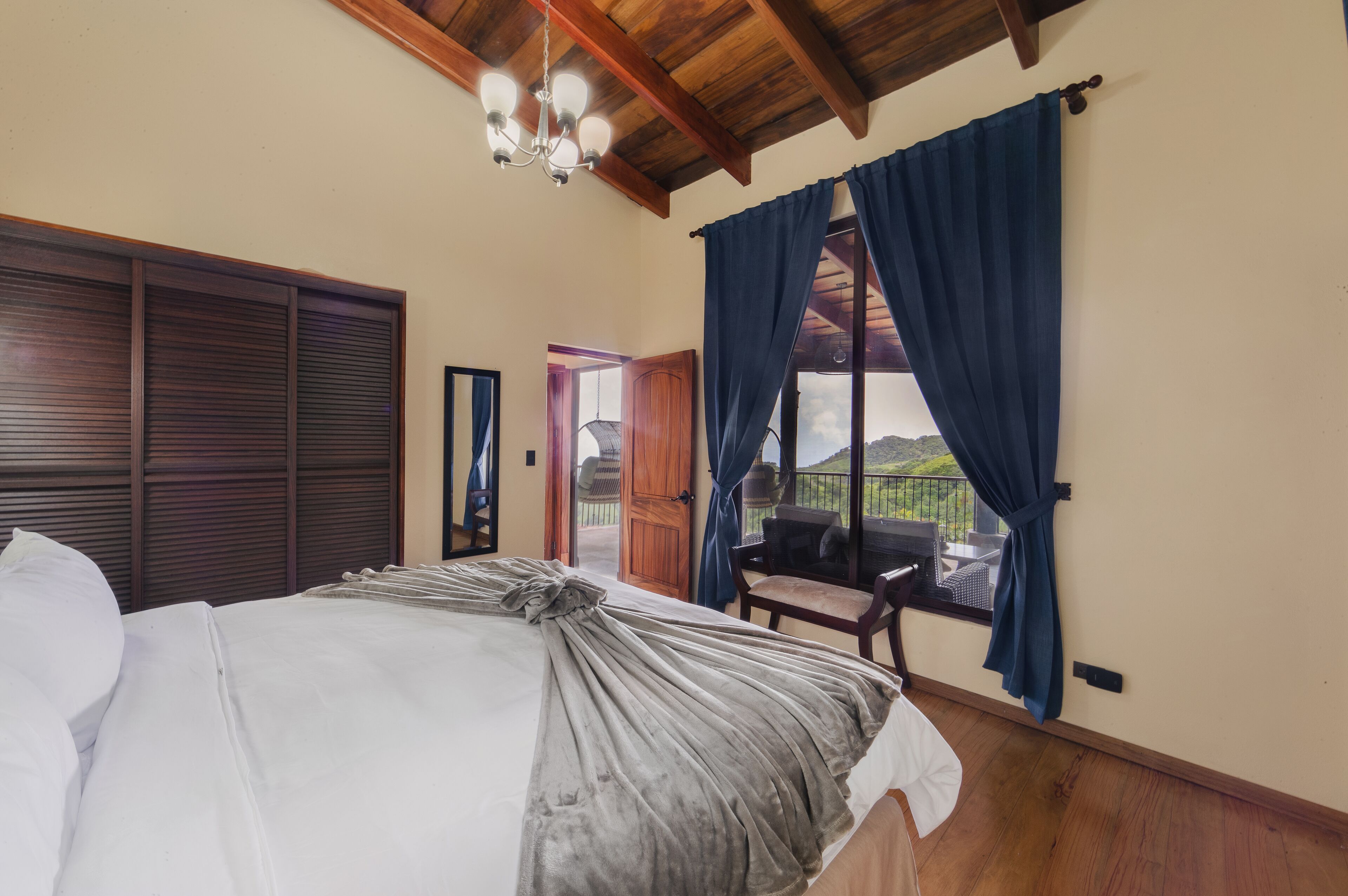 Une chambre à coucher avec un lit, des poutres en bois au plafond, une fenêtre avec des rideaux et une vue sur l’extérieur.