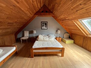 Een slaapkamer met een schuine kap, een bed, een stoel, nachtkastjes en een raam.