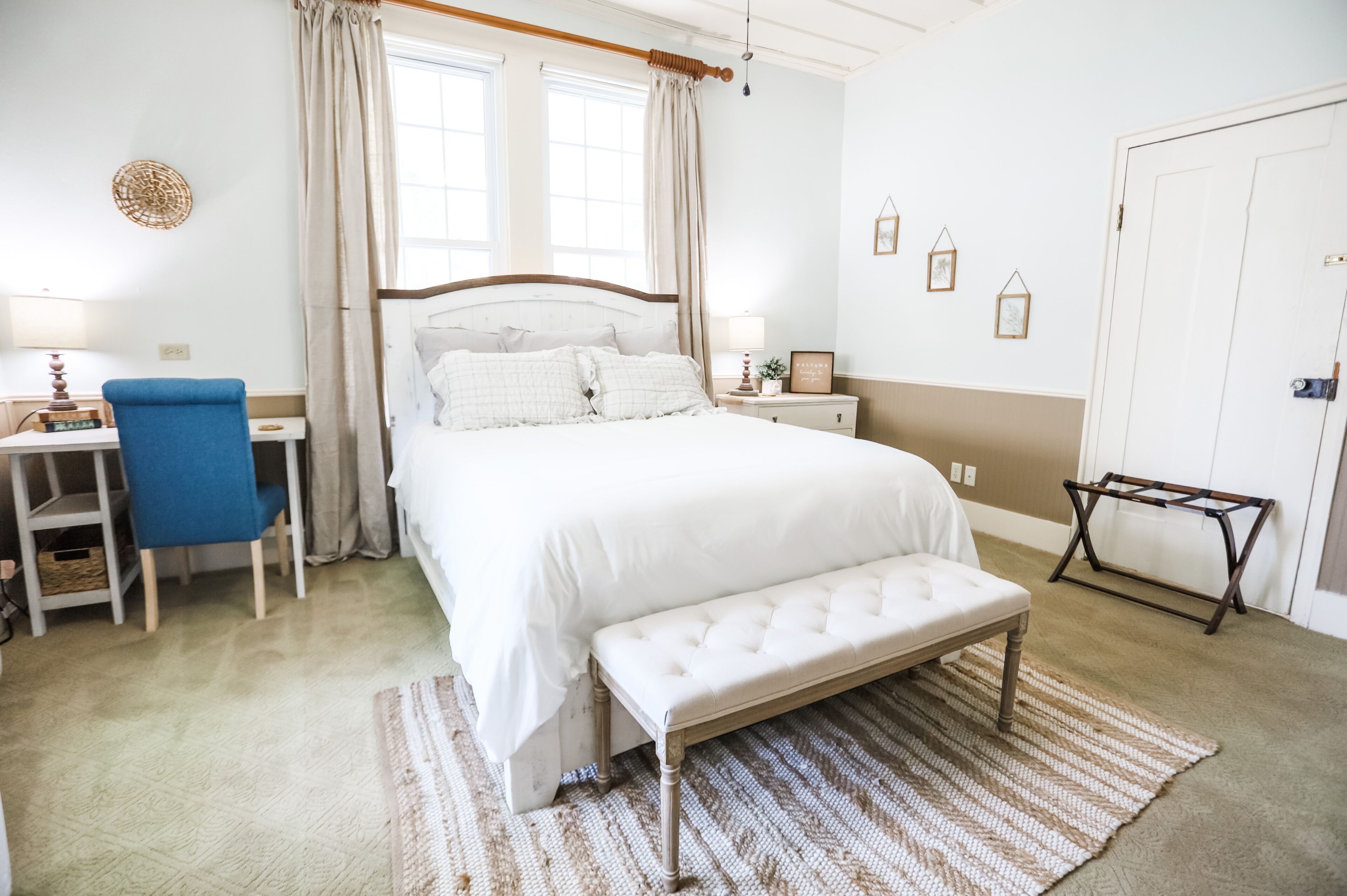Een slaapkamer met een groot bed, een bureau met stoel, een bankje en een kleine tafel met lamp.