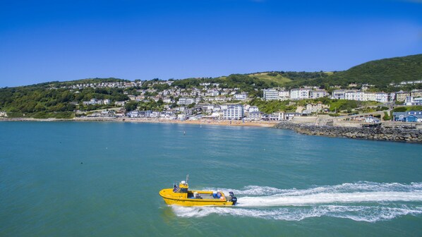 A coastal town with a yellow boat on the water, buildings on the shore, and a hilly backdrop. - Villa Amanti Apartment - an apartment that sleeps 4 guests in 2 bedrooms (Ventnor)