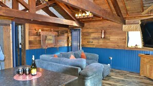 A cozy room with a wooden ceiling, a blue accent wall, a sectional sofa, and a small table with a bottle and glasses. - Tawitawoo Lodge Felmoor Park (Morpeth)