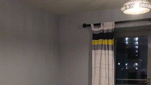 Un soggiorno con televisore a schermo piatto, poltrone arancioni e gialle, pavimento in legno scuro e una porta scorrevole in vetro con tende.
