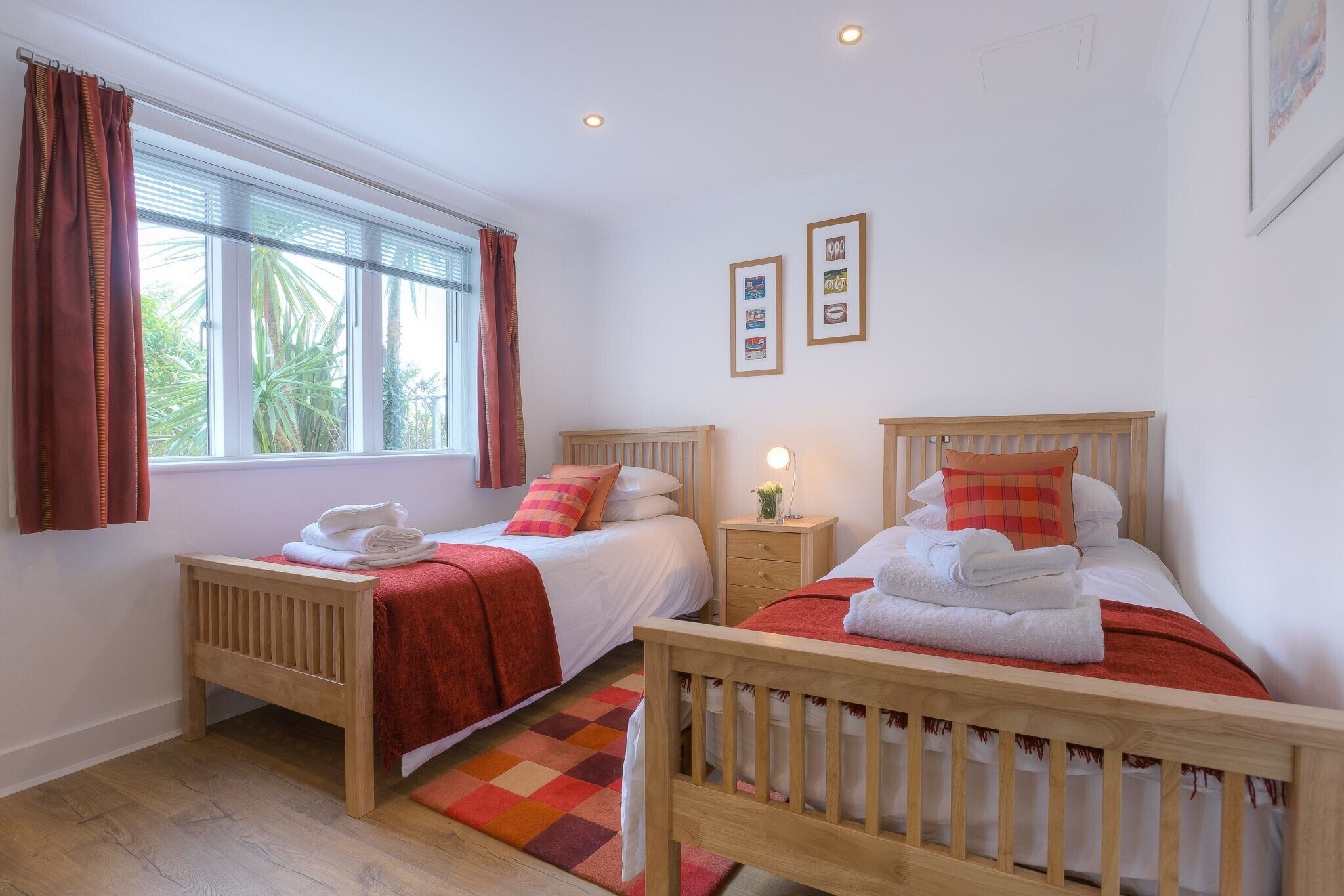 Une chambre avec deux lits en bois, une fenêtre avec des rideaux, une table de chevet avec une lampe et un petit tapis.