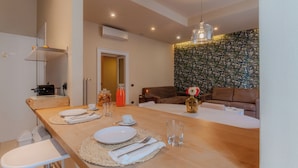 A modern dining area with a wooden table set for two, a brown leather couch, and a floral wallpaper accent wall. - Italianway - The B Village New (Milan)