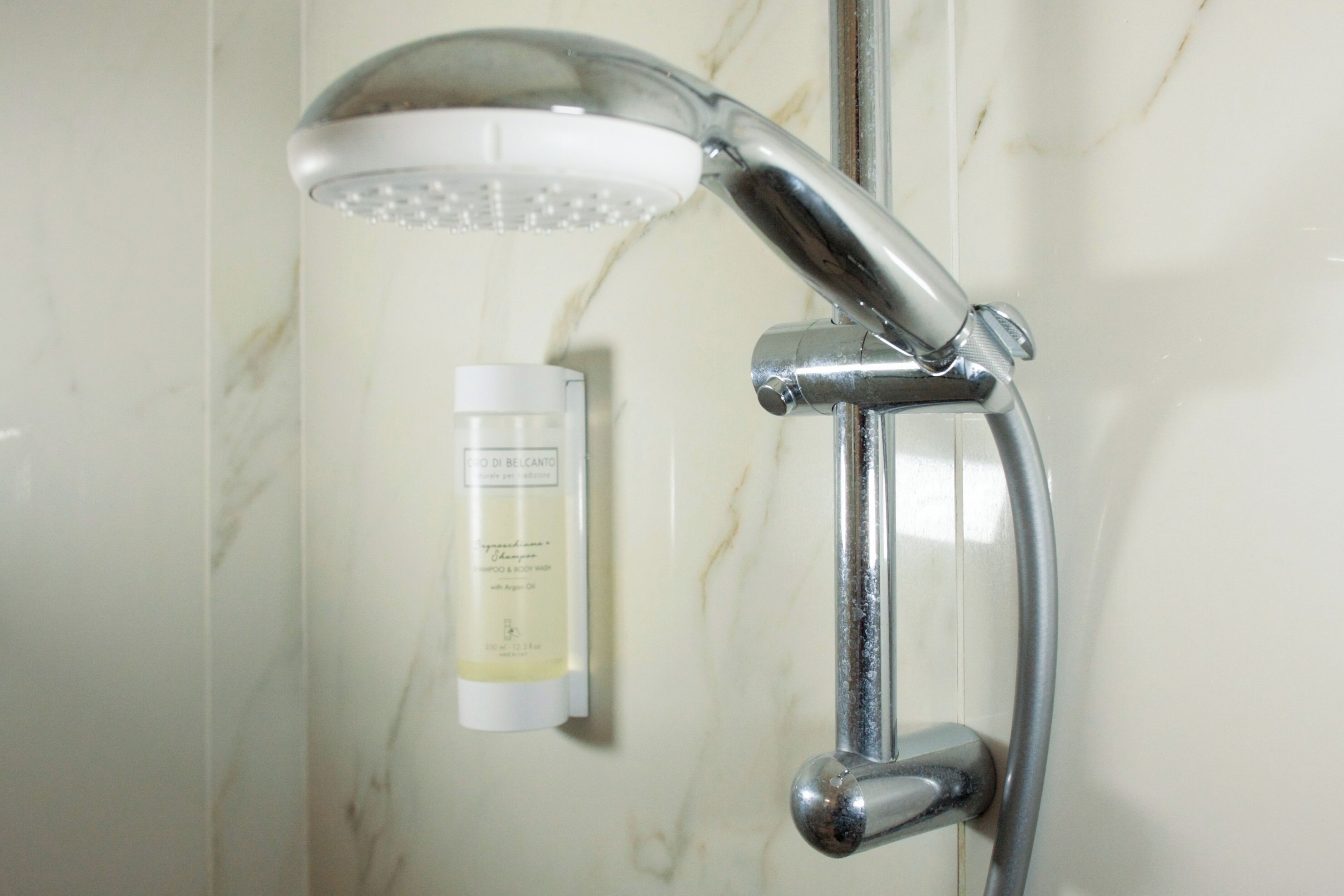 A shower with a handheld showerhead and a bottle of shampoo on the wall.