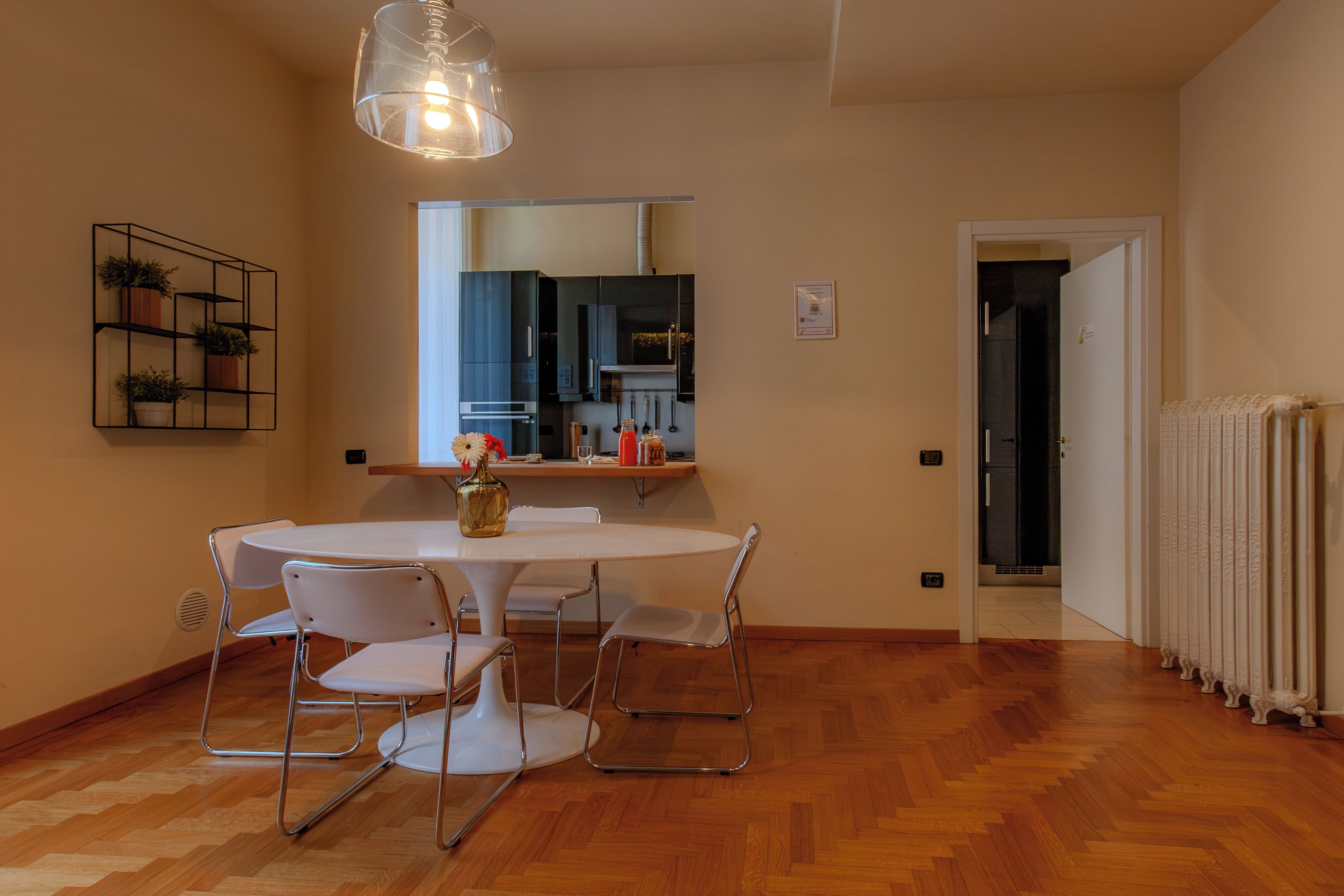 Een eetruimte met een ronde tafel en vier stoelen, een hanglamp, een spiegel boven de tafel, en een radiator op de vloer.