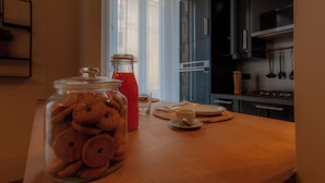 A kitchen with a wooden table, a glass jar of cookies, a red bottle, and a modern stove. - Italianway - The B Village New (Milan)