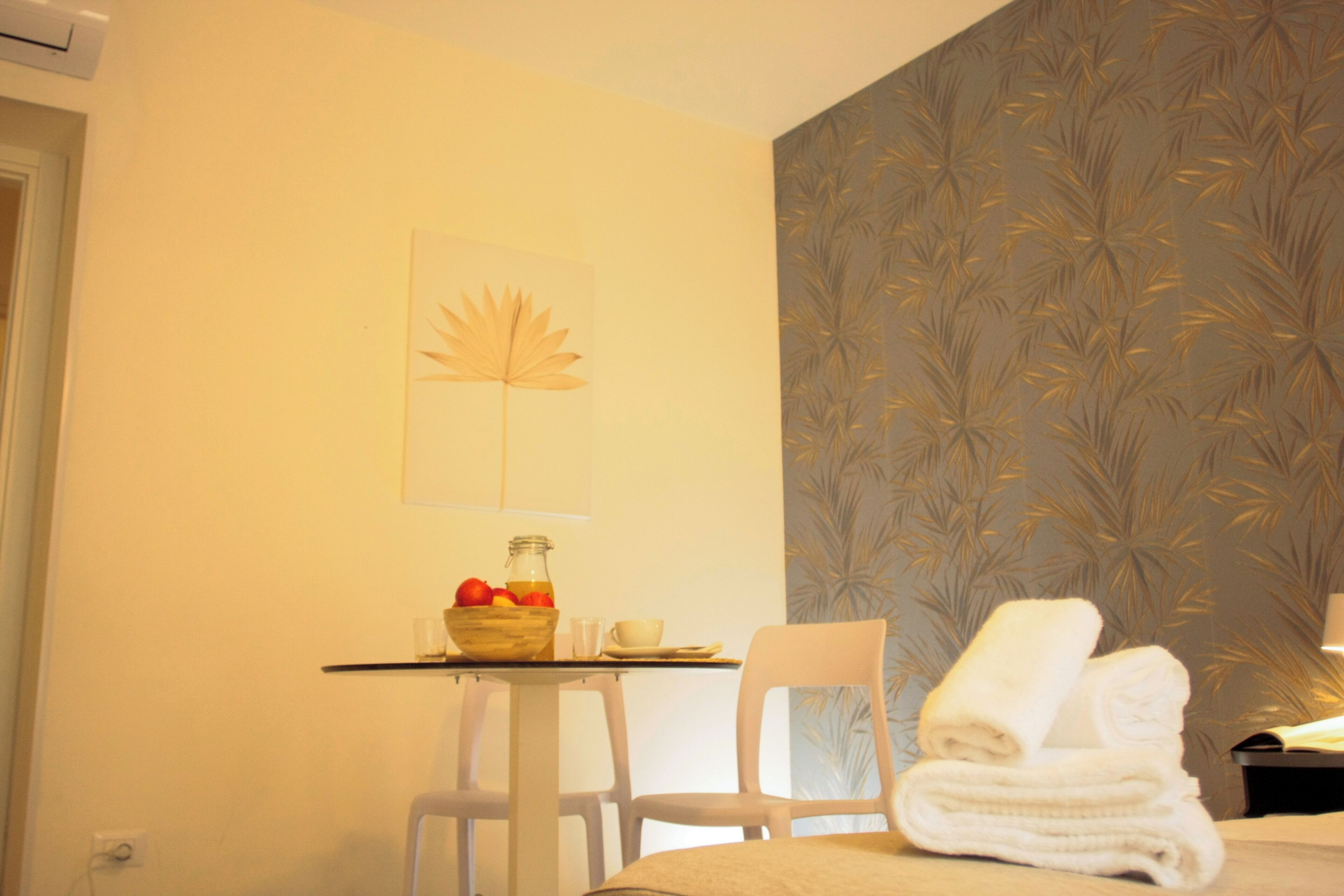Hotelkamer met een bed, een tafel met een fruitschaal, een stoel en een wand met een bladmotief.
