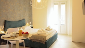 A hotel room with a bed, a table with breakfast items, a bowl of fruit, and a hanging light fixture. - Italianway - The B Village New (Milan)