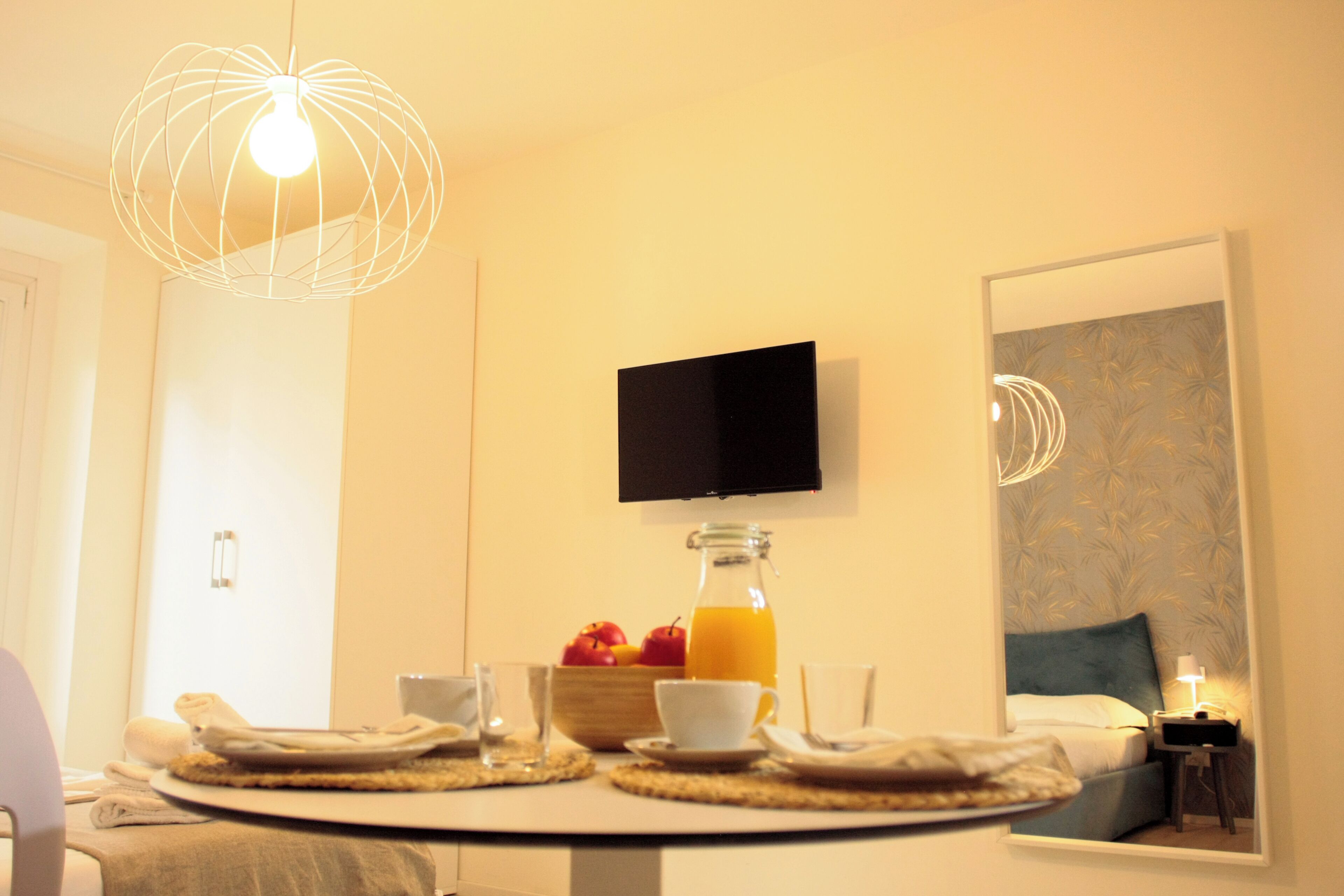 A breakfast setup with a bottle of orange juice, a bowl of fruit, and a flat-screen TV mounted on the wall.