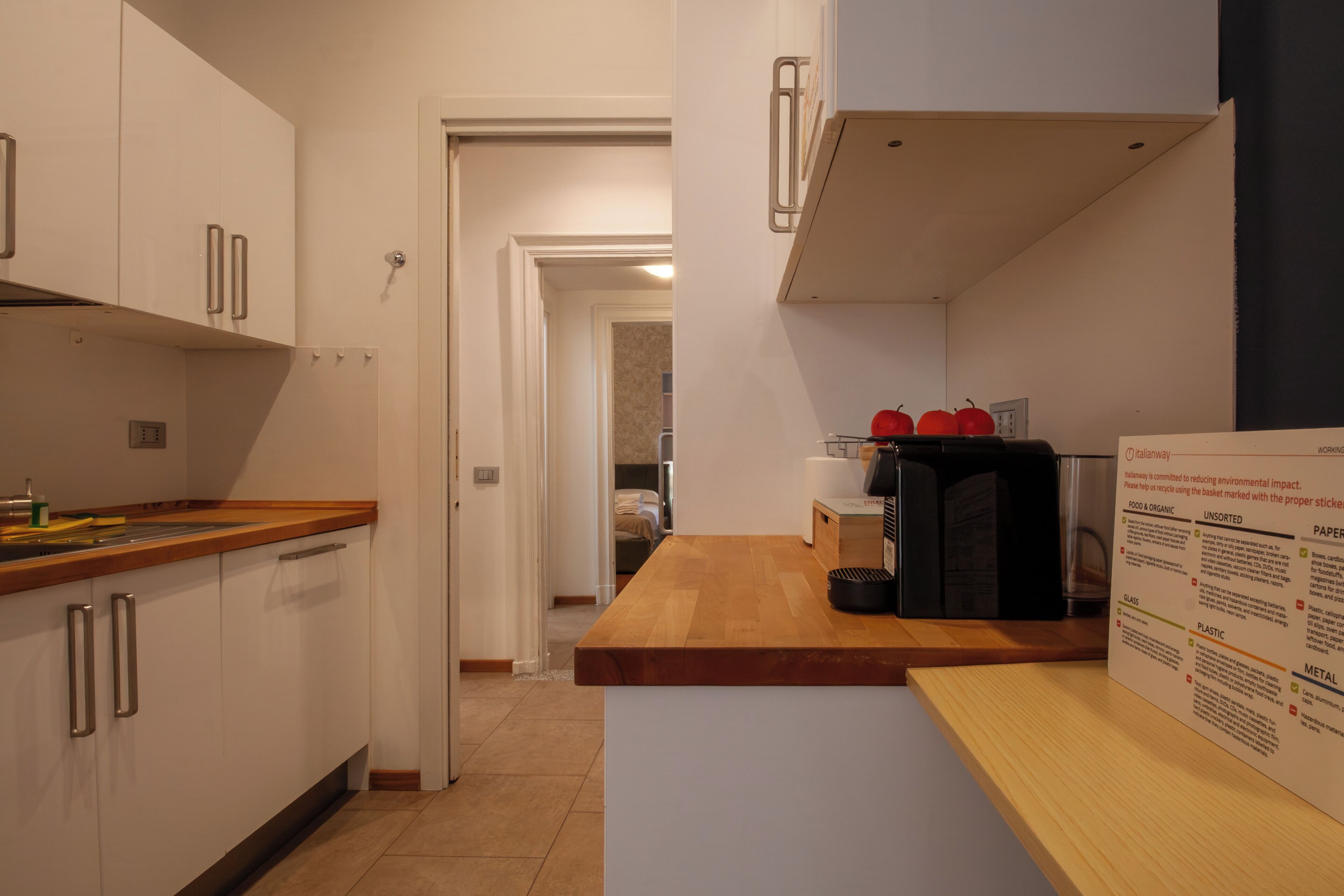 A modern kitchen with white cabinets, a wooden countertop, and a microwave. There is a sign on the counter with recycling information.