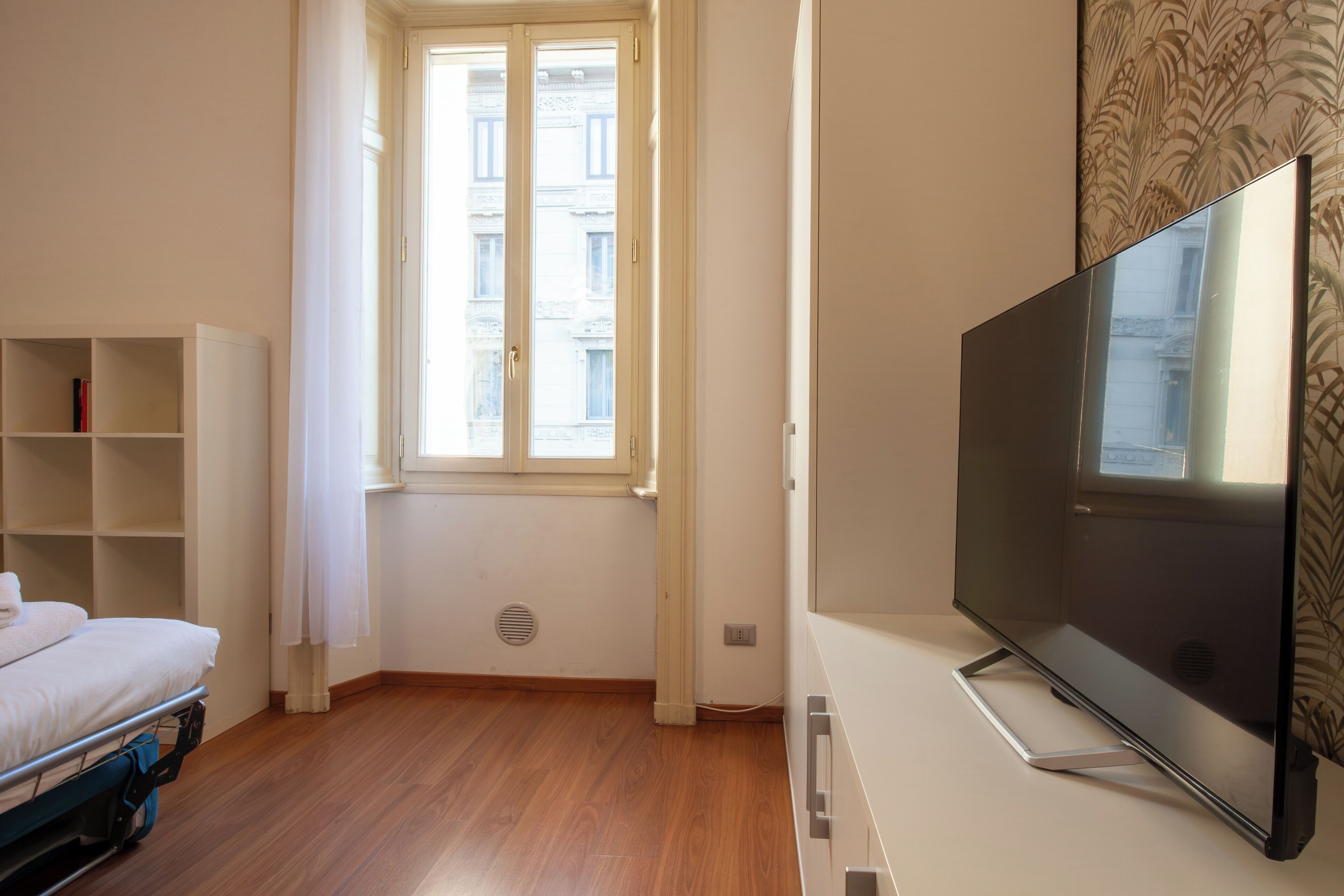 Una habitación con cama, televisión, ventana y estantería.