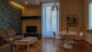 A modern living room with a sofa, coffee table, TV, and a dining area with chairs and a table. - Italianway - The B Village New (Milan)
