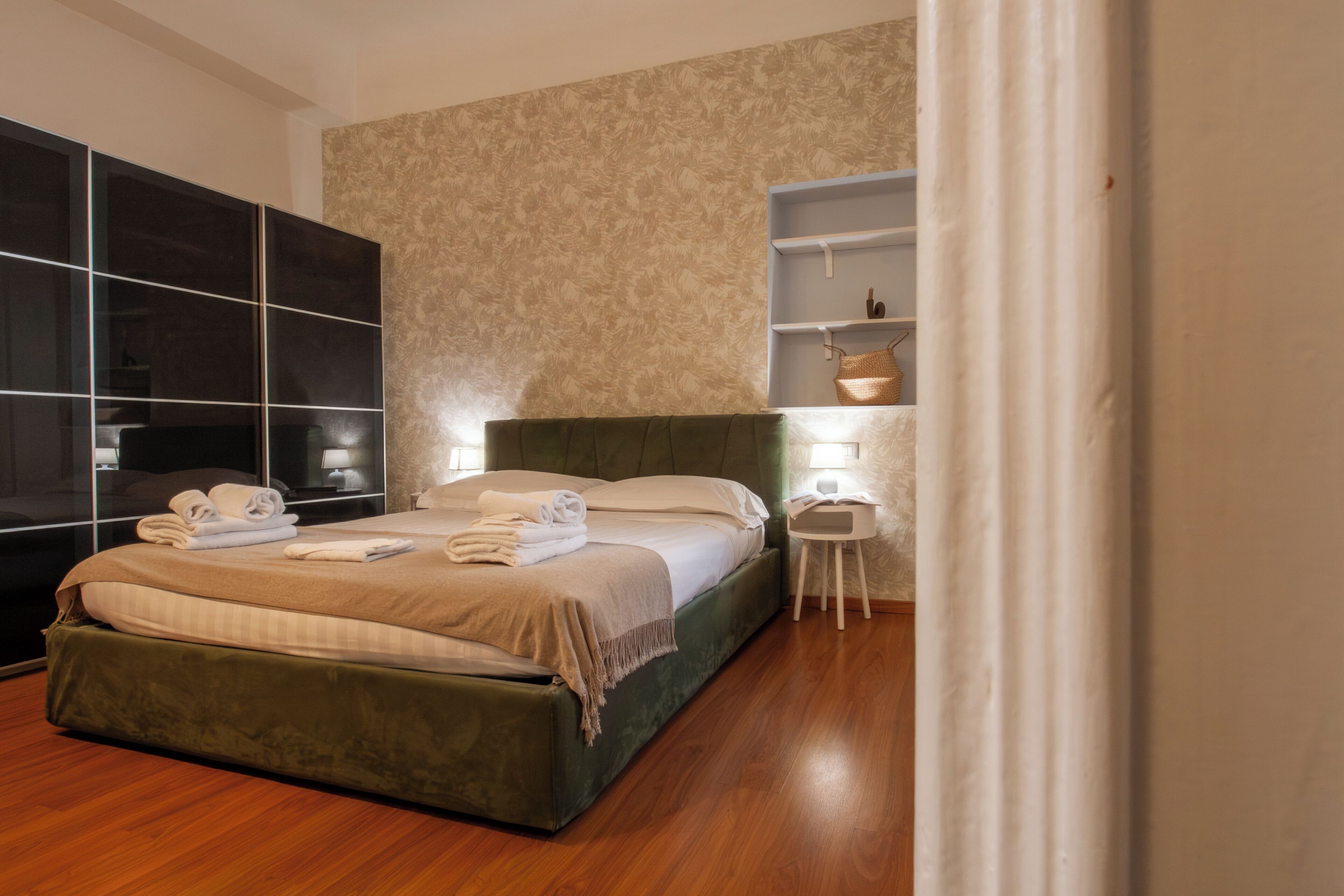 A modern bedroom with a large bed, a wardrobe, and a small bedside table.