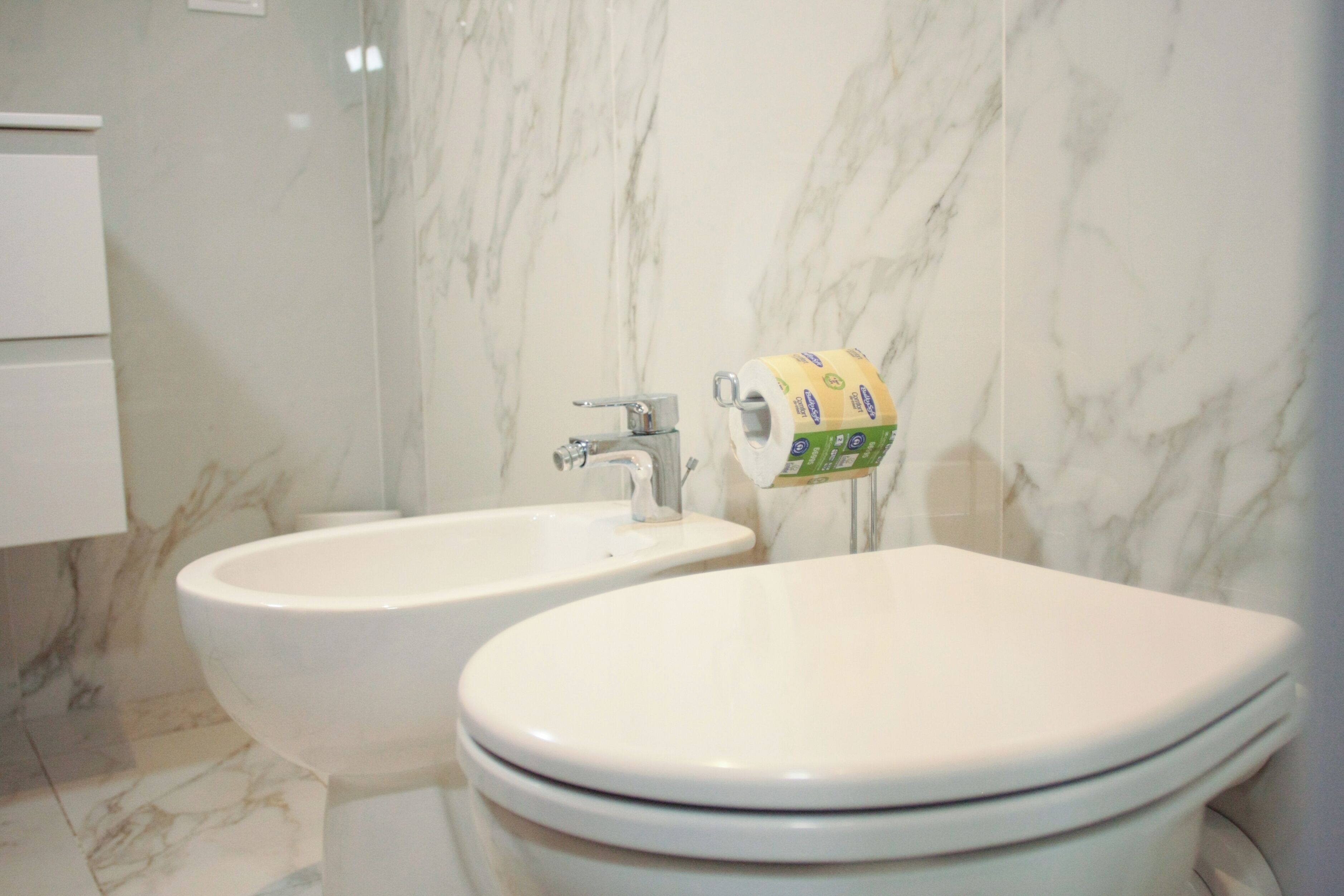 A bathroom with a bidet, a toilet, and a marble wall.