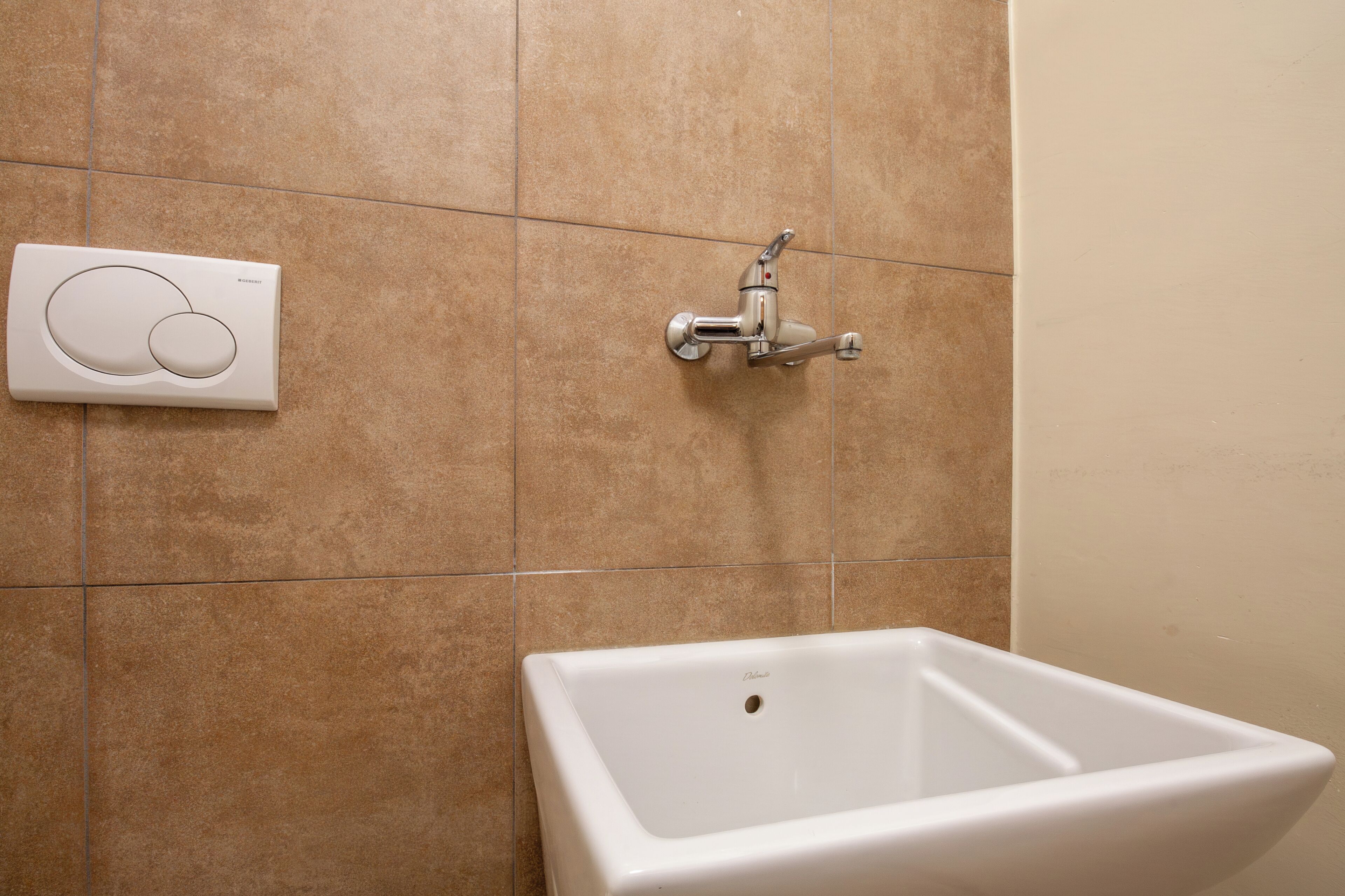 A bathroom with a white sink, a wall-mounted faucet, and a control panel.