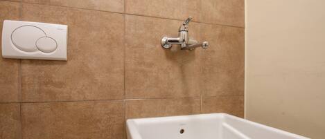 A bathroom with a white sink, a wall-mounted faucet, and a control panel.