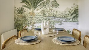 A dining table set with blue plates, wine glasses, and a white vase centerpiece, surrounded by wicker chairs. - Very Nice 60m² With Balcony Near The Beaches! (Six-Fours-les-Plages)
