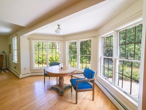A spacious room with large windows, a round wooden table, and two blue chairs. - Renovated, Five Bedrooms In Historic Williamstown (Williamstown)