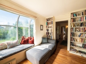 A cozy reading nook with a built-in bench by a large window, a bookshelf filled with books, and a view of greenery outside.