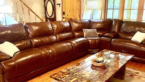 A living room with a brown leather sectional sofa, a wooden coffee table, and a patterned rug.
