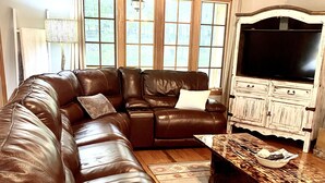 A brown leather sectional sofa with a matching ottoman, a wooden coffee table with a bowl, and a white cabinet with a TV.