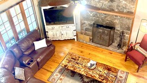 A cozy living room with a stone fireplace, a brown leather sofa, and a wooden ceiling.