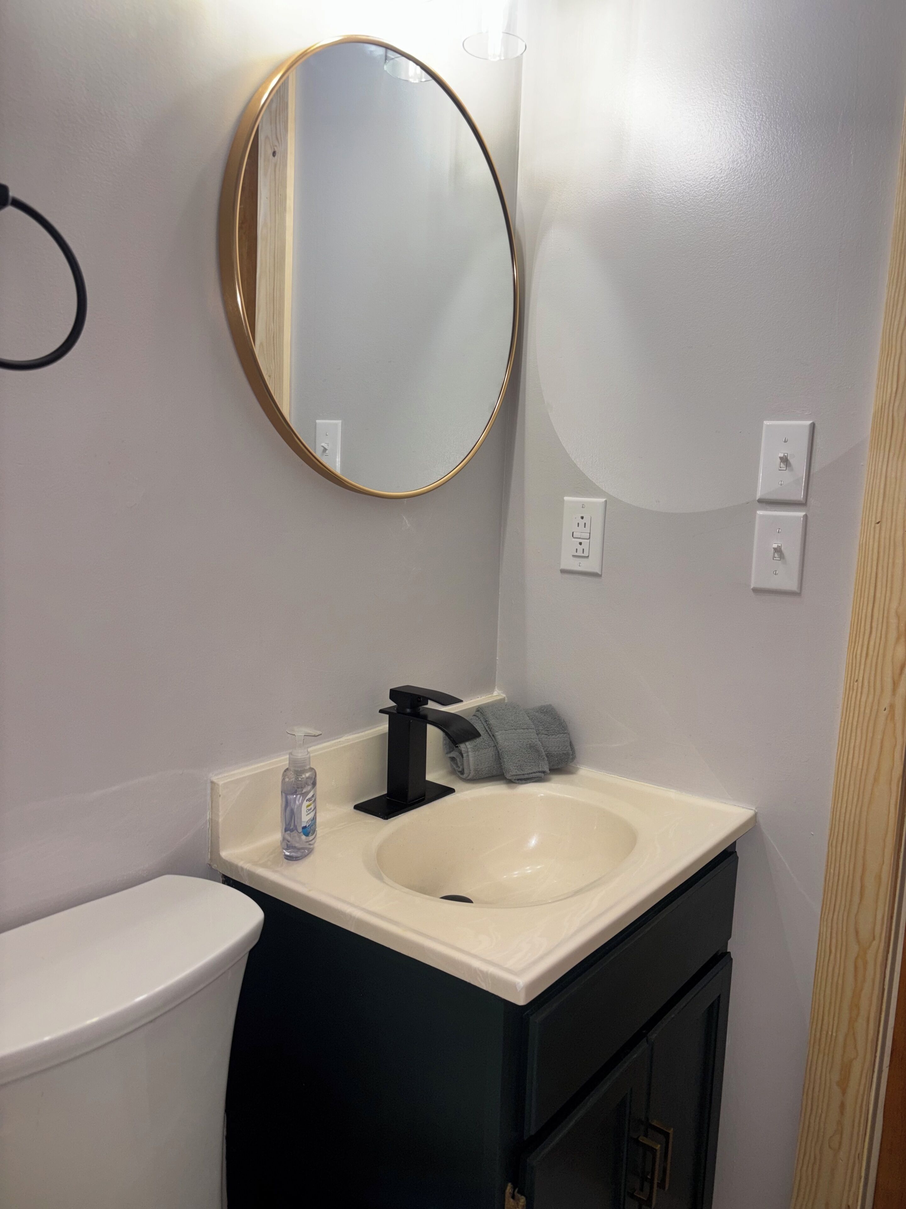 A bathroom with a white sink, black faucet, and a round mirror on the wall.