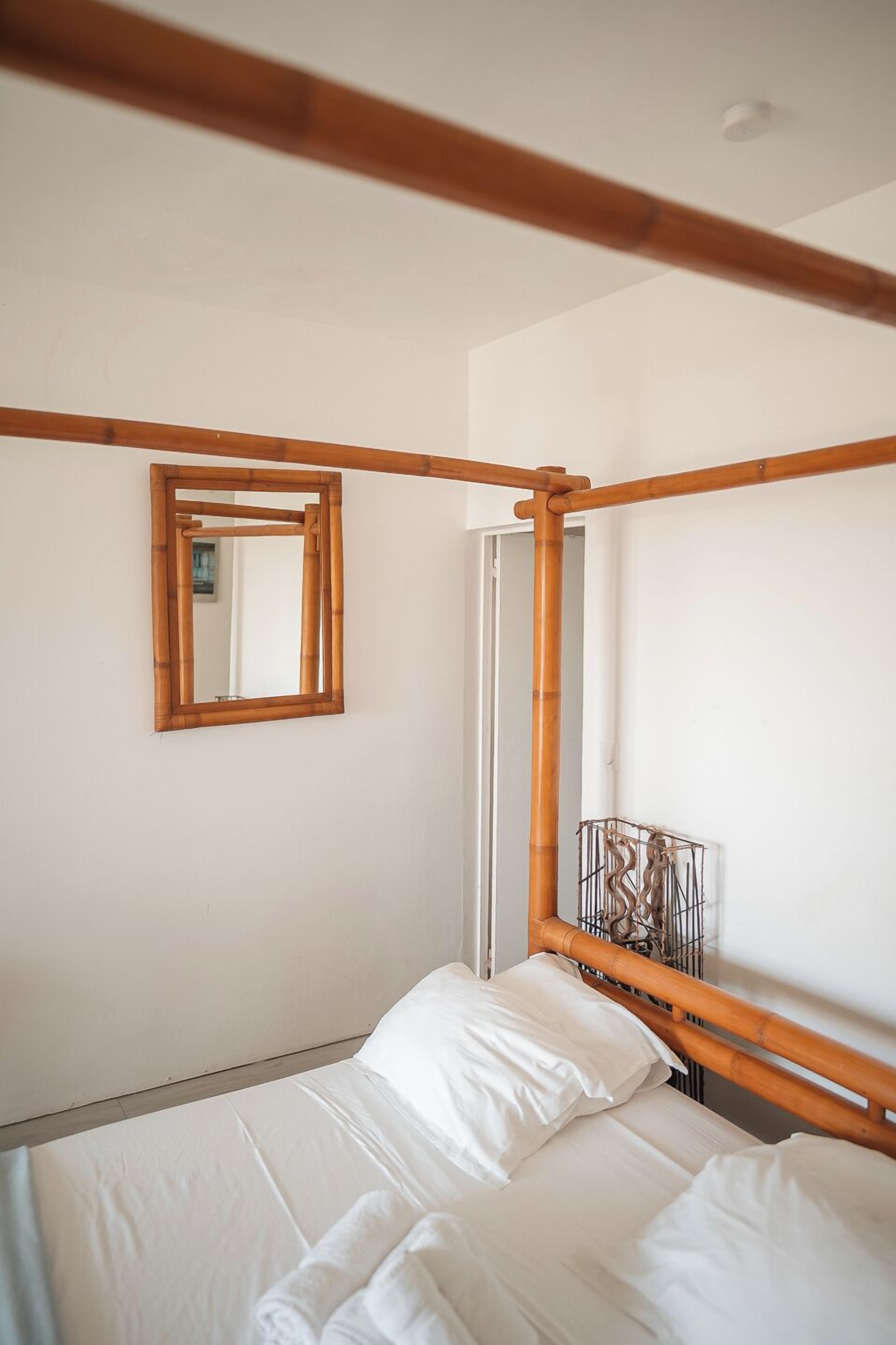 Una cama con ropa de cama blanca, un cabecero de madera, un espejo y una jaula de metal en la pared.