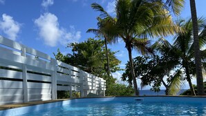 A clear blue pool with a white fence and palm trees in the background. - Le M Hotel Marie Galante (Capesterre-de-Marie-Galante)