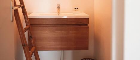 Une salle de bain avec un meuble-lavabo en bois, un miroir avec un éclairage intégré, un plancher en bois et un escabeau en bambou.