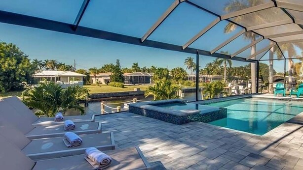 A covered outdoor swimming pool with lounge chairs and a view of a residential area. - VRCC Villa Skyfall (Cape Coral)