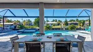 A poolside dining area with a table set for two, overlooking a swimming pool and a view of a residential area. - VRCC Villa Skyfall (Cape Coral)