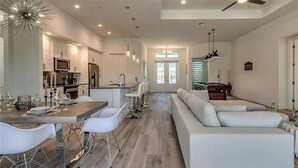 A spacious living area with a dining table, white sofas, and a kitchen in the background. - VRCC Villa Skyfall (Cape Coral)