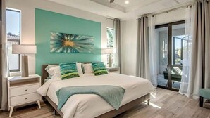 A bedroom with a bed, a nightstand, a lamp, and a view of the outdoors through a sliding door. - VRCC Villa Skyfall (Cape Coral)