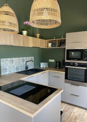 A modern kitchen with a black induction cooktop, stainless steel appliances, and wooden cabinetry.