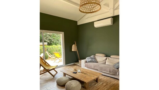A living room with a wooden floor, a sofa, a coffee table, and a wicker chair. - Maison Cocooning Proche Plages (Soustons)