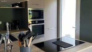 A modern kitchen with a central island, two hanging wicker pendant lights, and a view of the outdoors. - Maison Cocooning Proche Plages (Soustons)