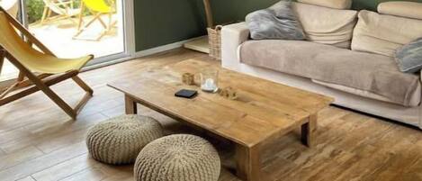 Un salon avec un plancher en bois, un canapé, une table basse et un fauteuil en osier.