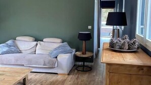 A living room with a sofa, a coffee table, a lamp, and a decorative pine cone arrangement. - Maison Cocooning Proche Plages (Soustons)