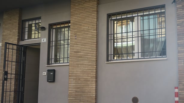 A building with a brick facade, a gated entrance, and two windows with metal bars.