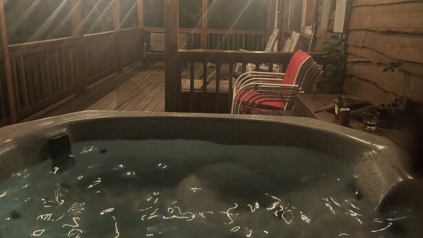 A hot tub in a wooden deck area with string lights overhead.