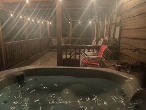Un bain à remous installé sur une terrasse en bois, avec des guirlandes lumineuses suspendues au-dessus.
