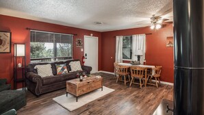 A living room with a brown leather sofa, wooden coffee table, and a dining area with wooden chairs and a table.