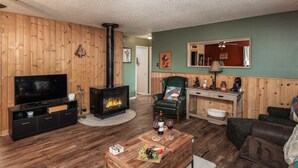 A cozy living room with a fireplace, wooden walls, a television, and comfortable seating.