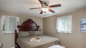 A bedroom with a wooden bed, a ceiling fan, and a bedside table with a tray of orange juice and a book.