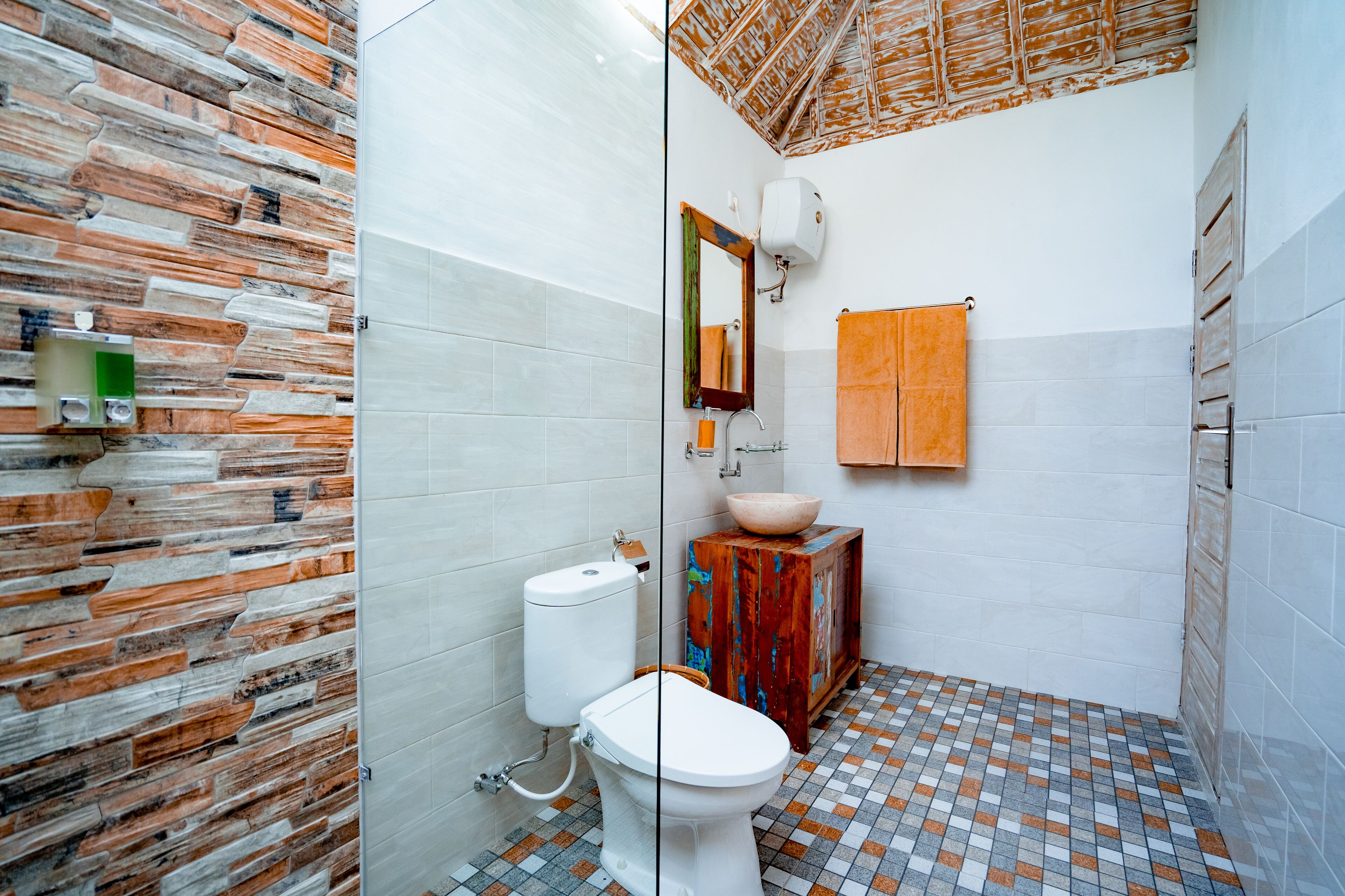 A bathroom with a stone wall, a toilet, a sink with a wooden cabinet, and a towel hanging on the wall.