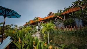 A resort with a stone staircase leading to a building with a tiled roof, surrounded by lush greenery and a clear sky. - Gara Gara Sea View (Penida Island)